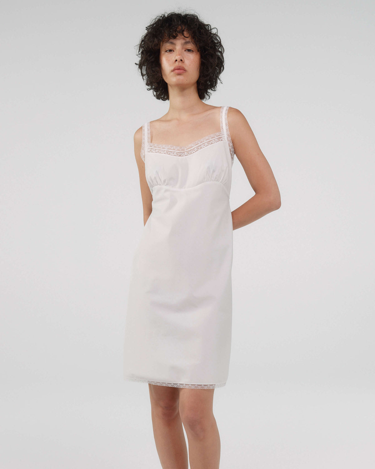 Woman wearing a white slip dress against a plain background