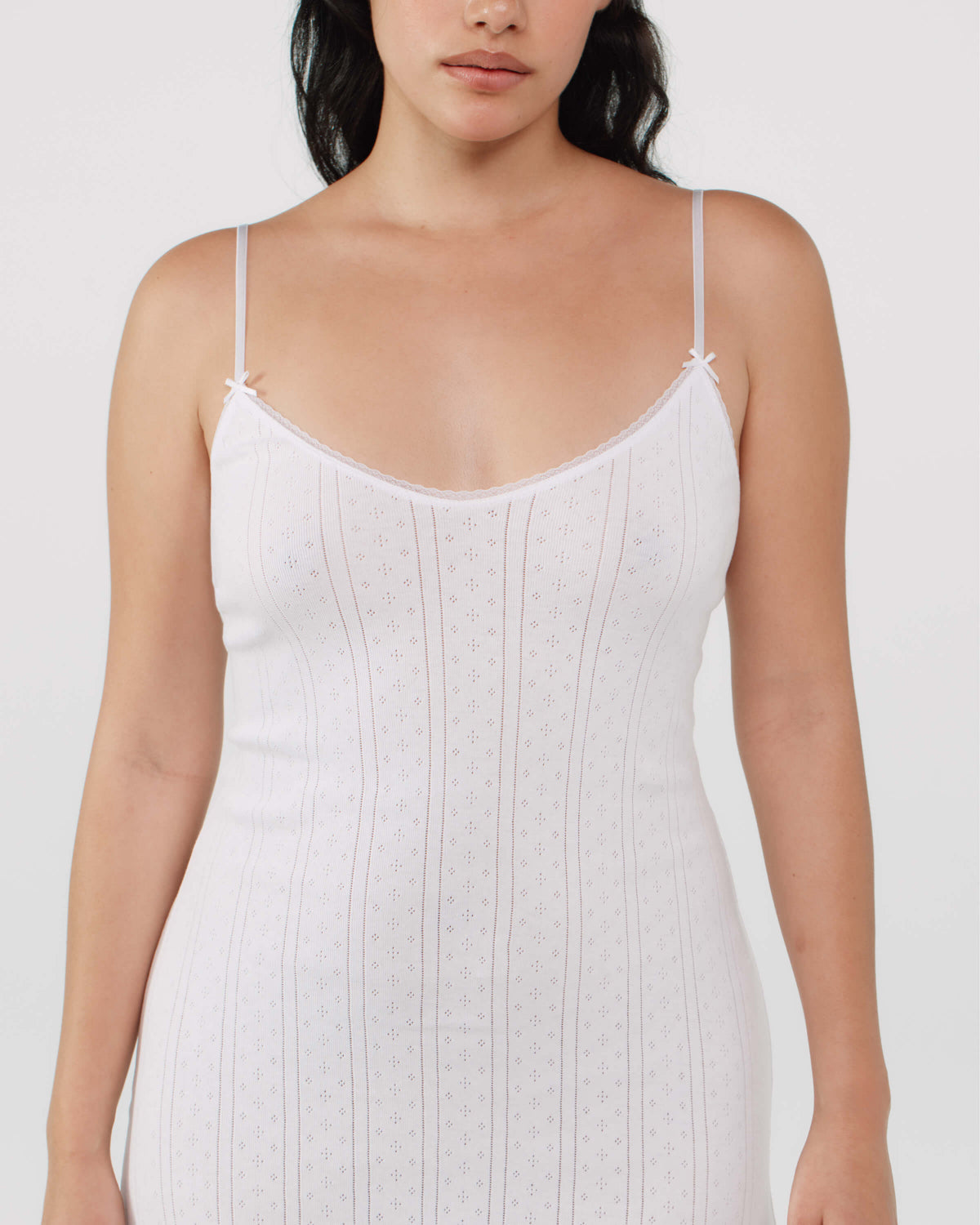 Woman wearing a white slip dress with thin straps on a plain background