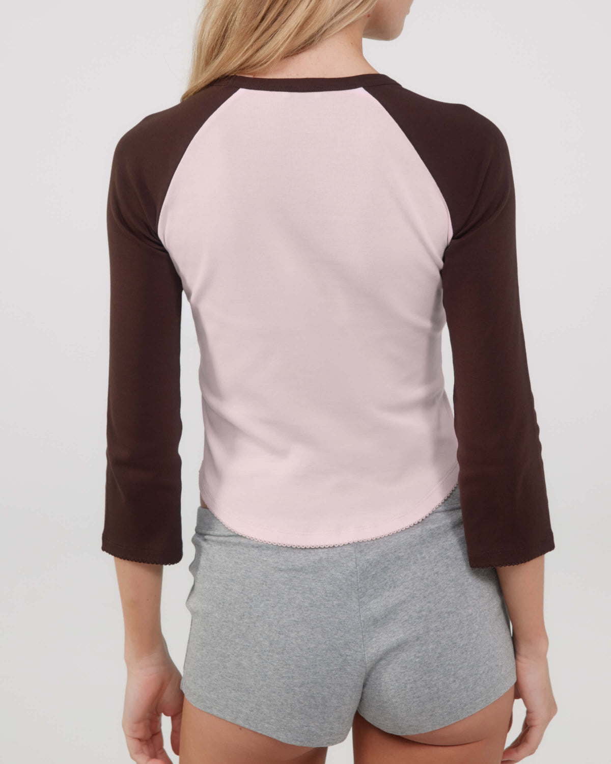 Person wearing a pink and brown long-sleeve top with gray shorts on a plain background