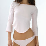 Woman wearing a light pink long-sleeve top and matching underwear on a light gray background