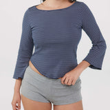 A woman wearing a navy blue and white striped three-quarter sleeve top with grey shorts, shown from the neck down against a plain white background.