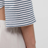 Close-up of a person wearing a white top with thin navy horizontal stripes and a scalloped hem, paired with white bottoms, against a plain light background.