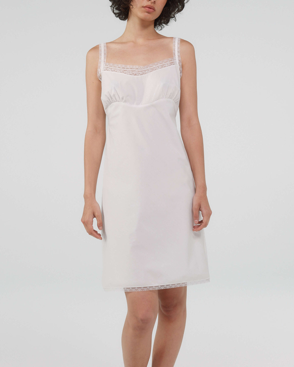 Woman wearing a white slip dress on a plain background