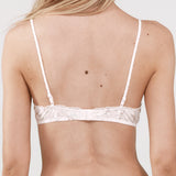 Woman wearing a white lace bralette with floral print. 